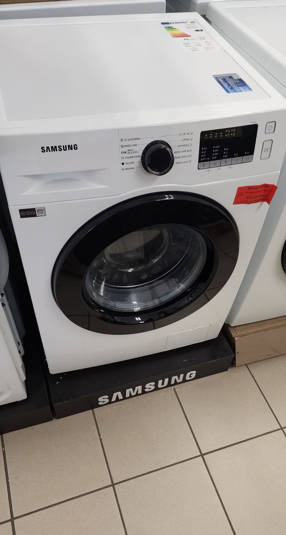 A white washing machine is sitting on a tiled floor in a store.