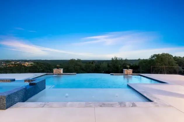 Infinity pool overlooking a green landscape at sunset, with a clear blue sky.