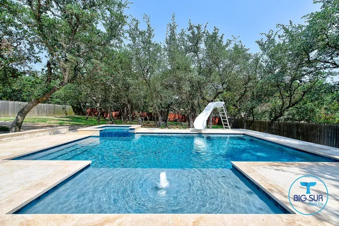 Backyard pool with blue water, fountain, and trees around a stone patio