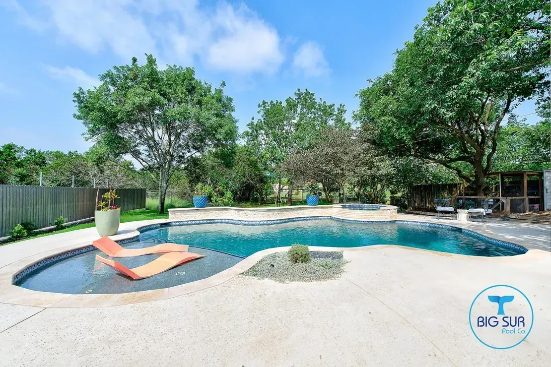 Backyard pool with a shallow sun shelf, orange lounge chairs, and trees under a blue sky