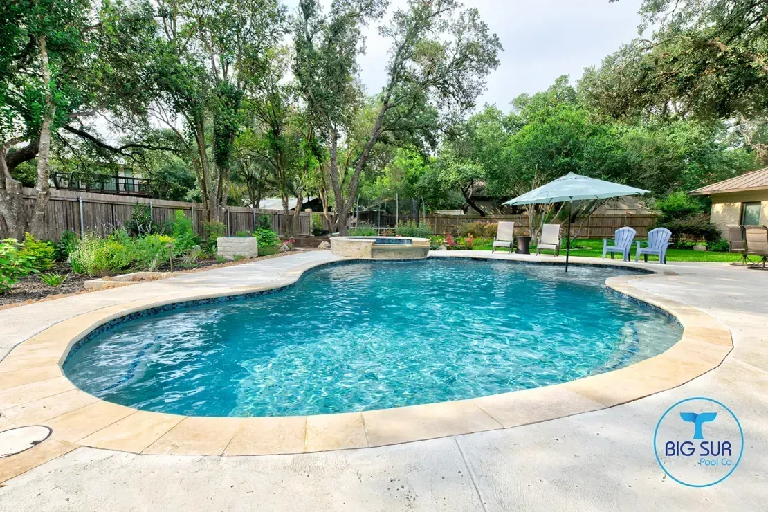 Outdoor swimming pool with blue water, stone deck, and lounge chairs under trees
