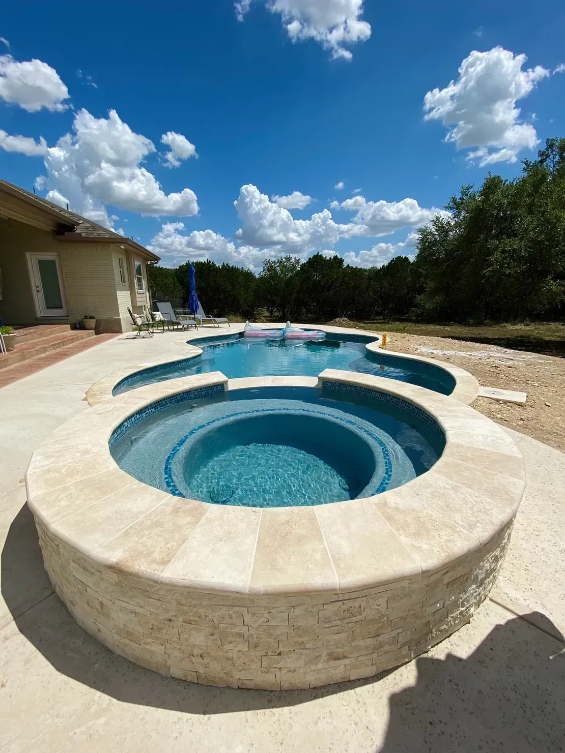 Backyard hot tub and swimming pool under a bright blue sky with clouds