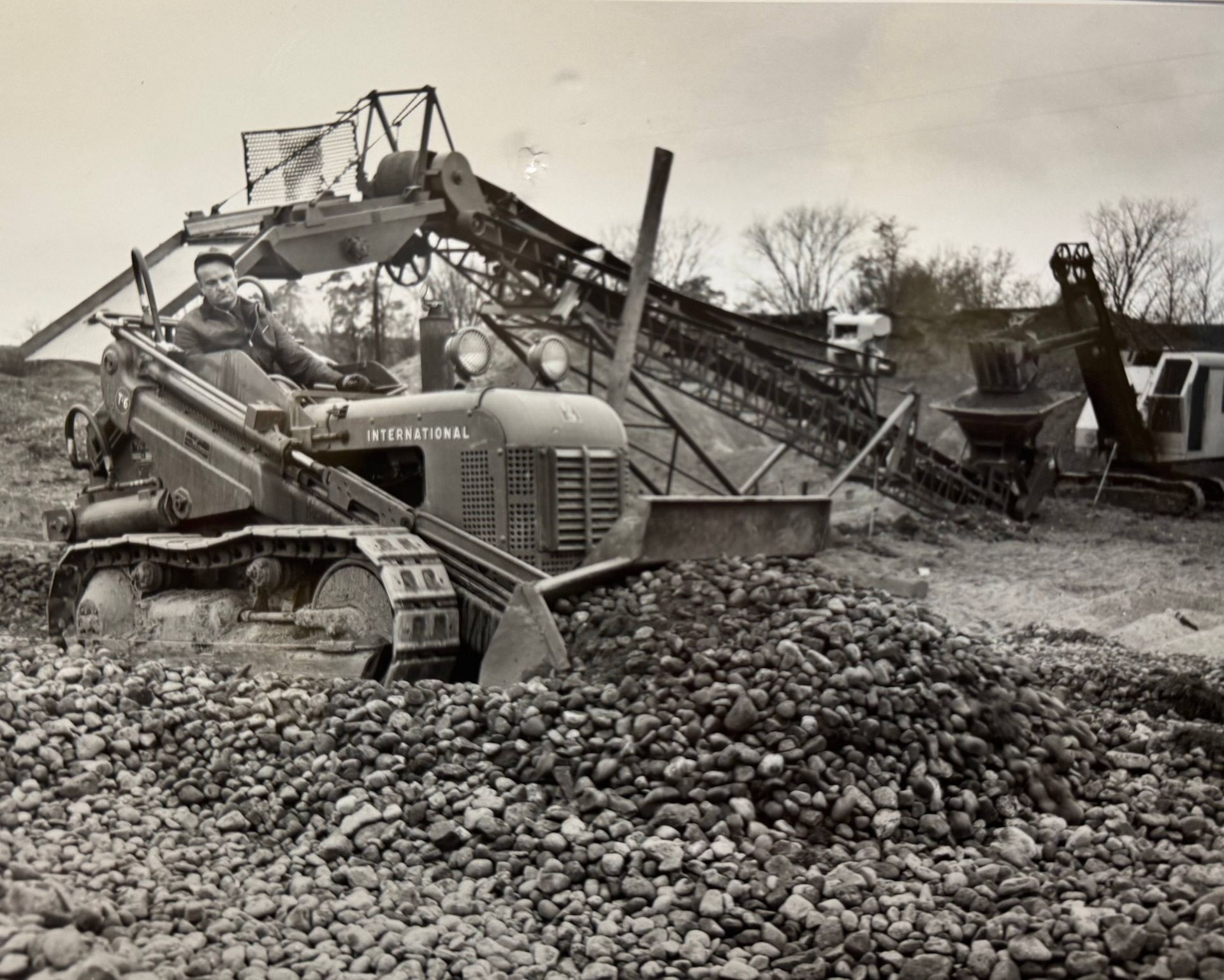 Man operating a vintage tractor, moving rocks near conveyor belts at a quarry.