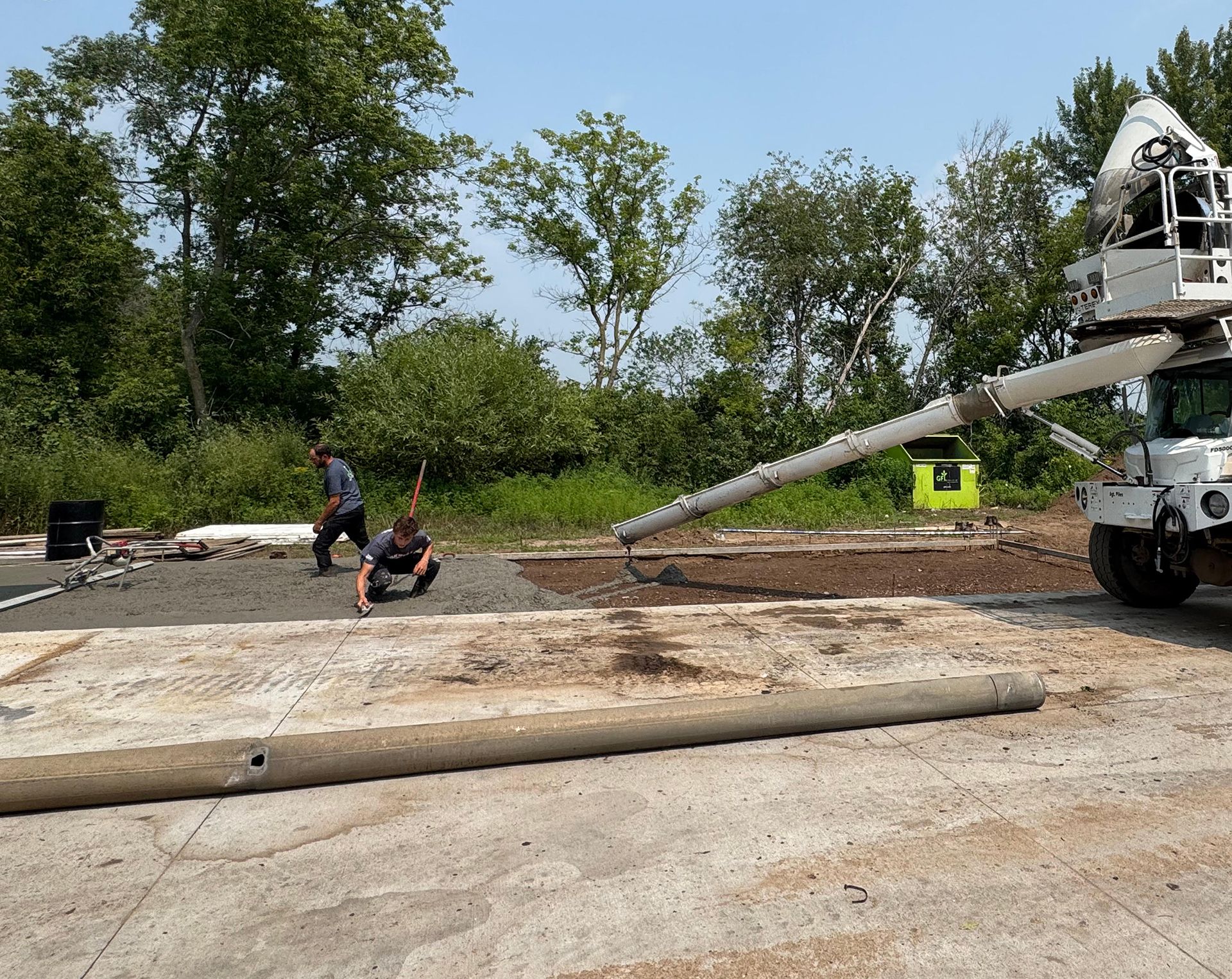 Construction workers pouring concrete on a site.  A truck with an extended arm is delivering the cement.