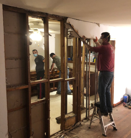 A man wearing a mask is standing on a ladder in a room.