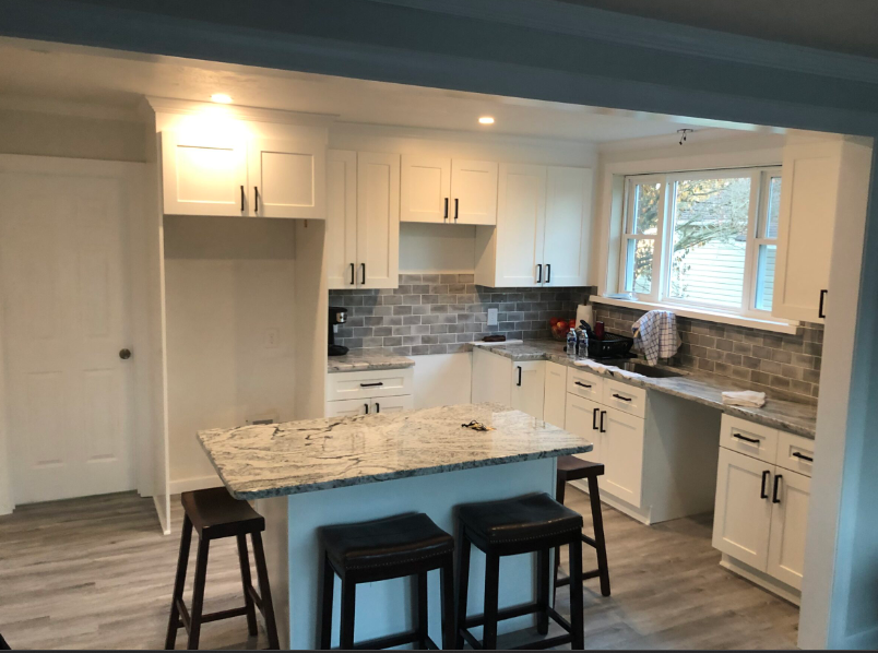 A kitchen with white cabinets , granite counter tops , and stools.