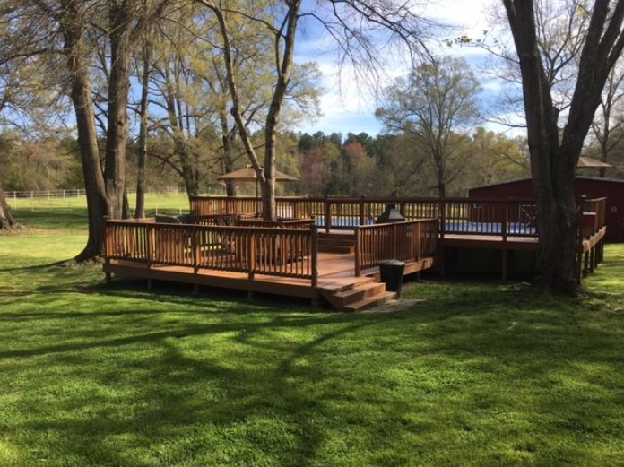 A large wooden deck in the middle of a lush green field surrounded by trees.