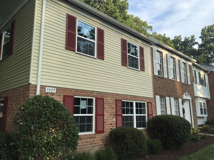 A brick house with white siding and red shutters