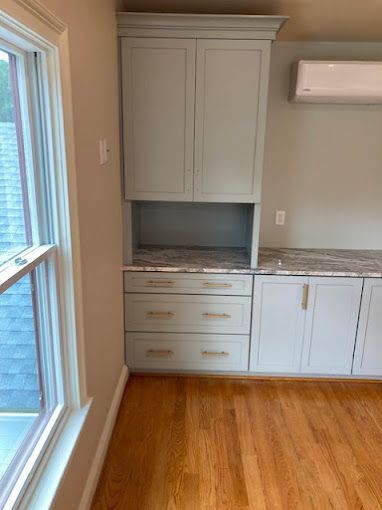 A kitchen with white cabinets and hardwood floors and a window.