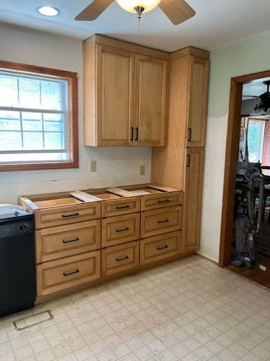 A kitchen with wooden cabinets and drawers and a ceiling fan.