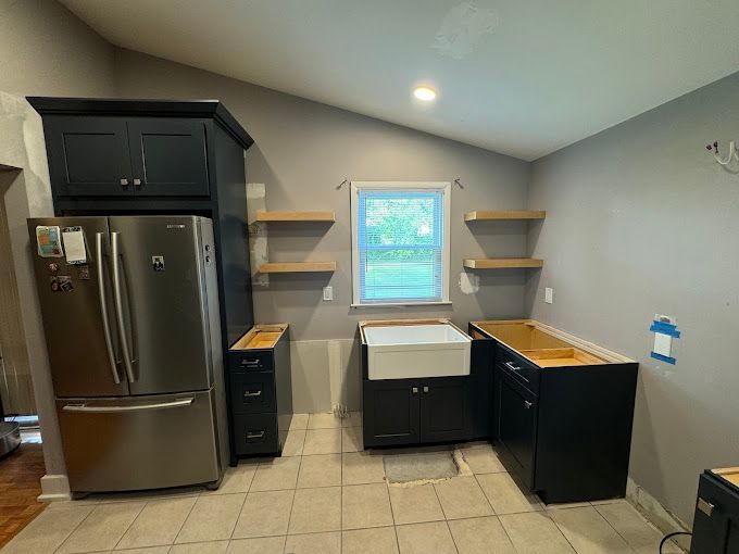 A kitchen with a refrigerator , sink , cabinets and shelves.