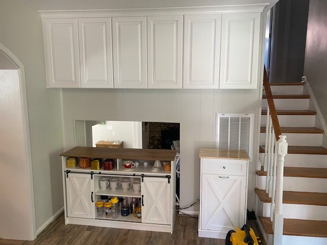 A kitchen with white cabinets and wooden stairs.
