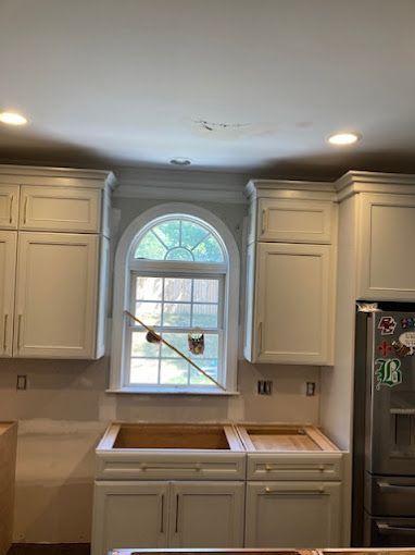 A kitchen with white cabinets , a sink , and a window.