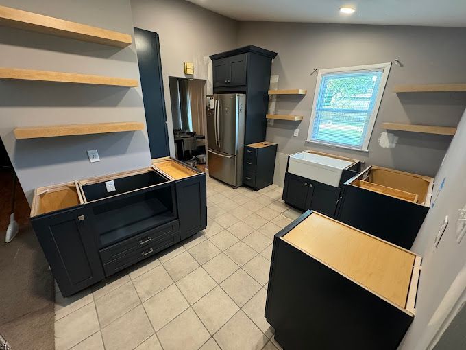A kitchen with black cabinets , a stainless steel refrigerator , a sink , and a window.