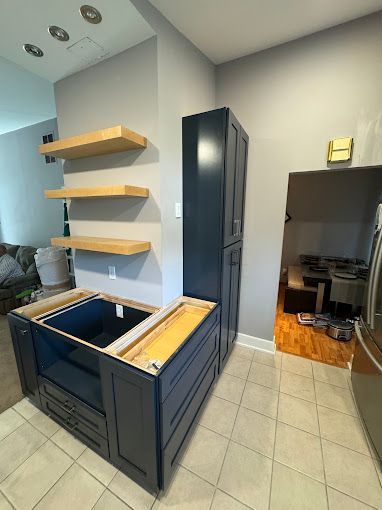 A kitchen with a sink , cabinets , shelves and a refrigerator.