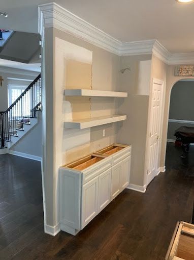 A living room with white cabinets and shelves and a staircase.