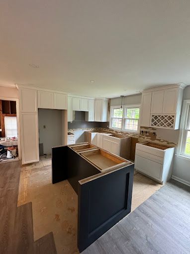 A kitchen under construction with white cabinets and a black island.