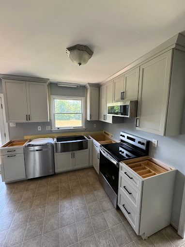 A kitchen with white cabinets , a stove , a sink , and a window.