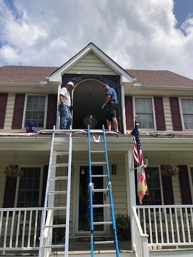 Two men are standing on a ladder in front of a house.