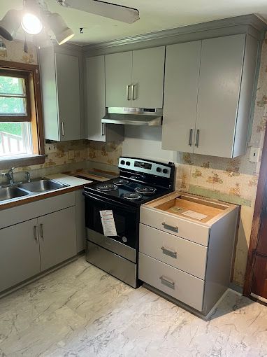 A kitchen with a stove , sink , cabinets and drawers.