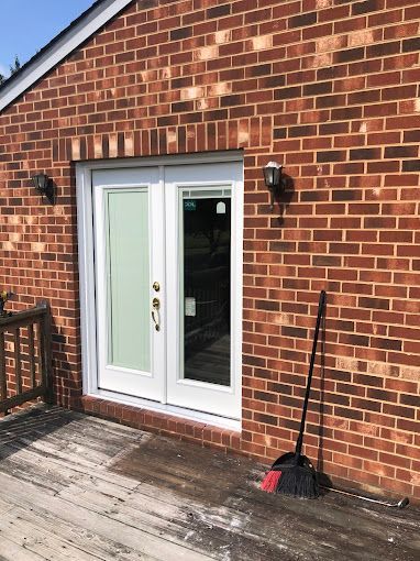 A brick building with a white door and a broom on the deck.