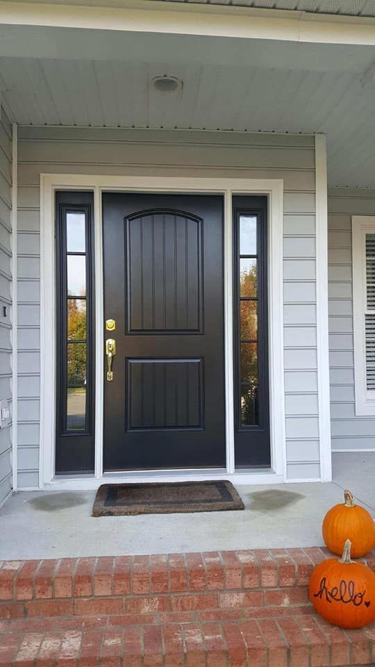 A black front door with two pumpkins on the porch of a house.