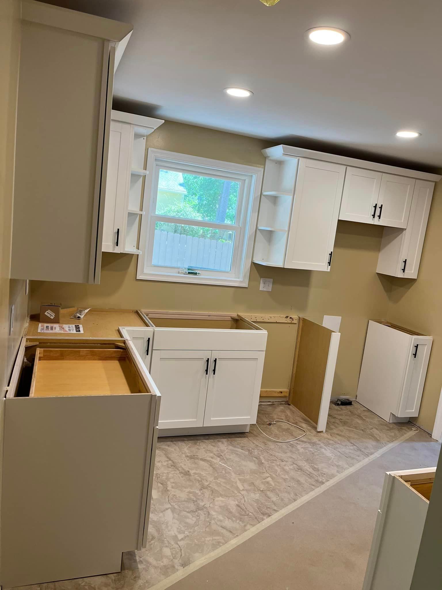 A kitchen is being remodeled with white cabinets and a window.