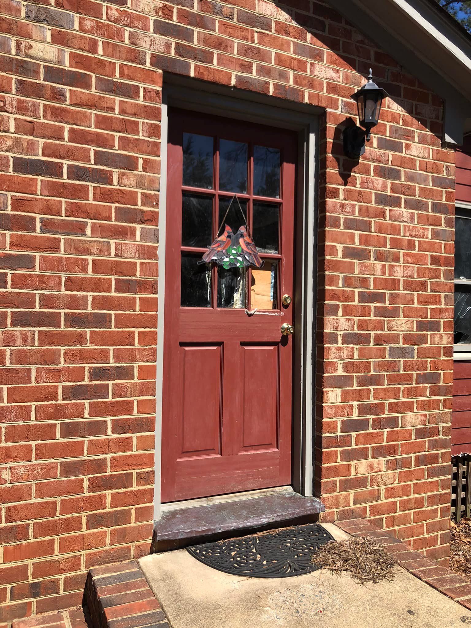 A red door with a wreath on it is on a brick building.
