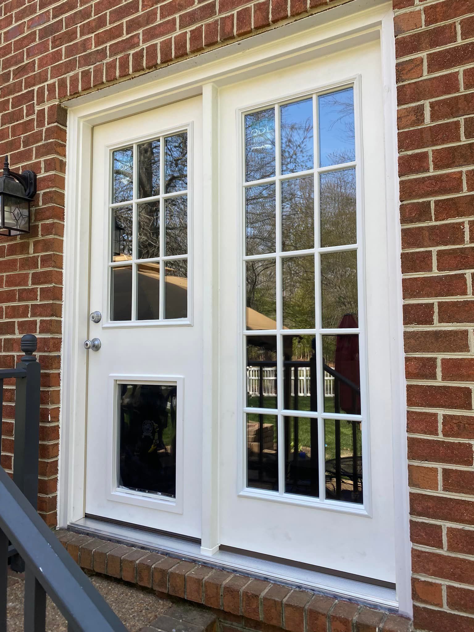 A white door with a dog door on the side of a brick building.