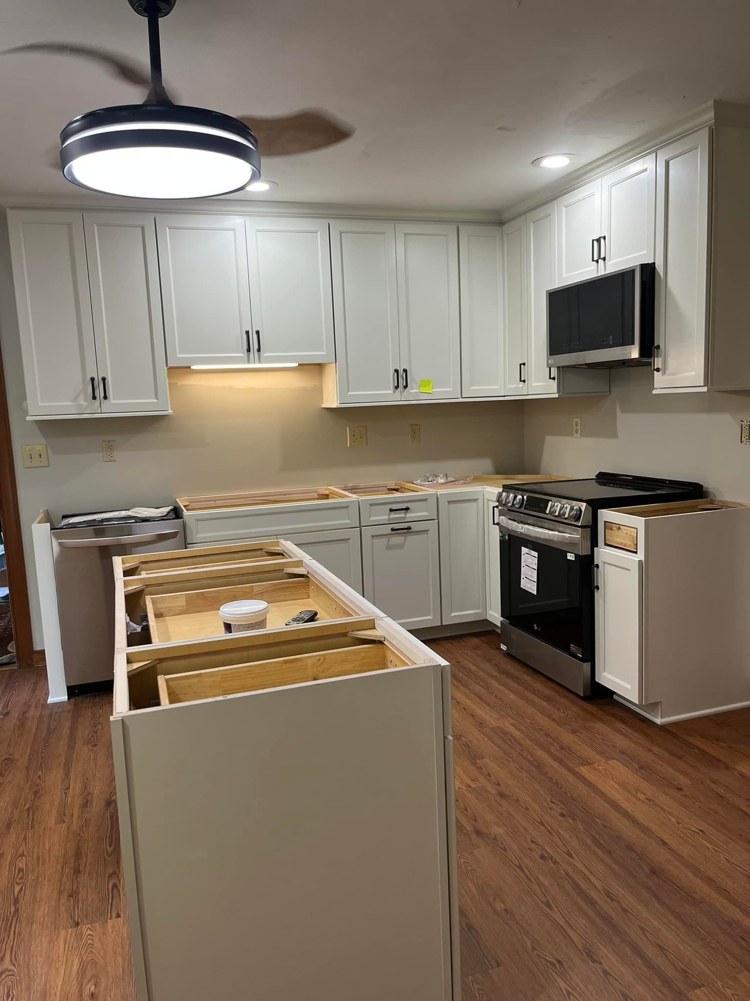 A kitchen with white cabinets , a stove , a microwave , and a ceiling fan.