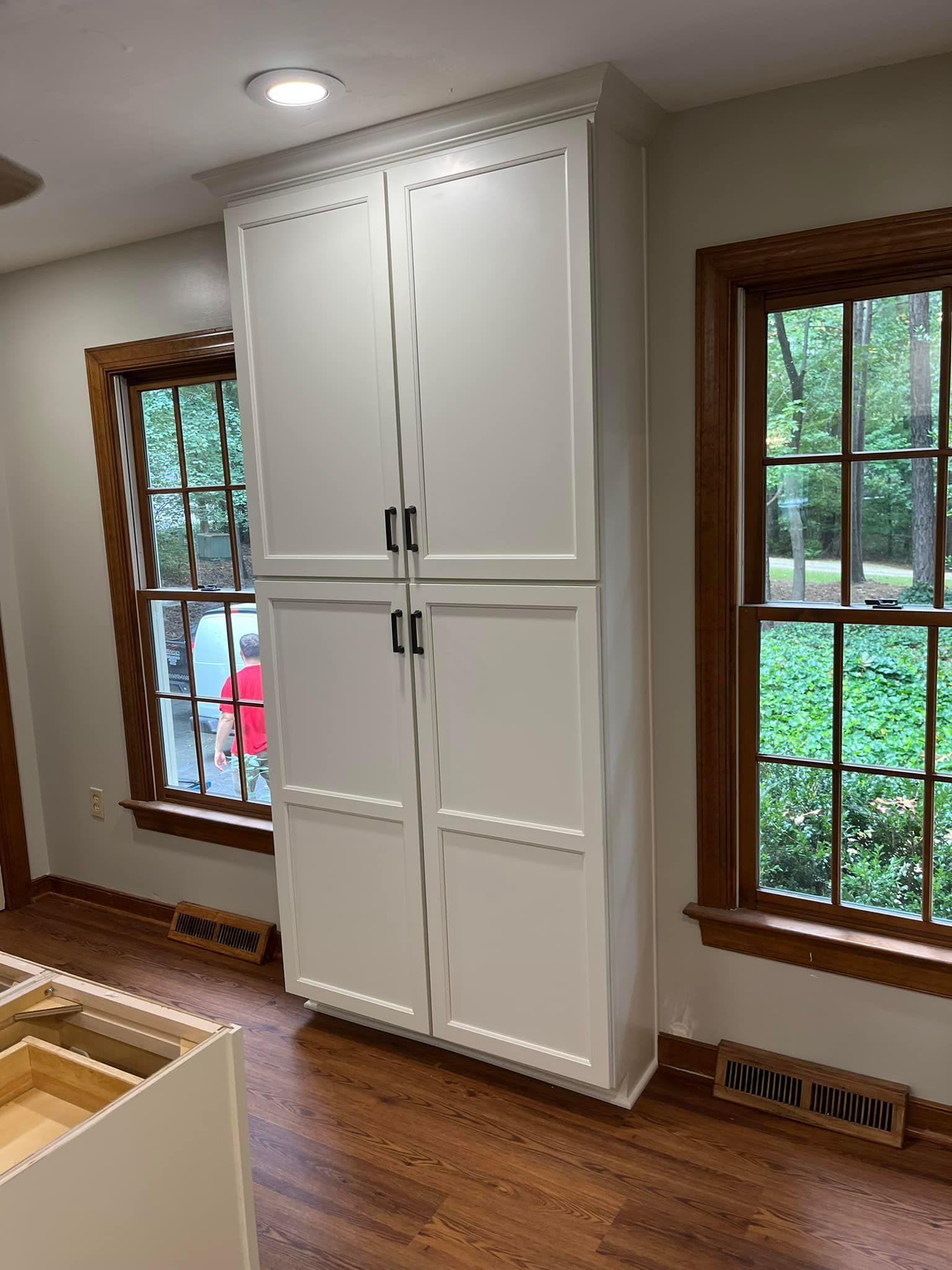 A white cabinet is sitting in a room next to two windows.
