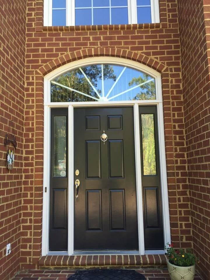 The front door of a brick house with a black door and a window.