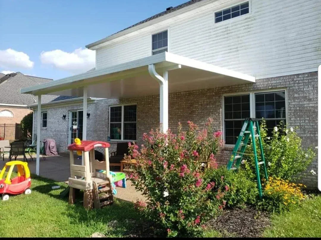 Backyard patio with a children's playset, shrubs, and a white brick house under a covered porch
