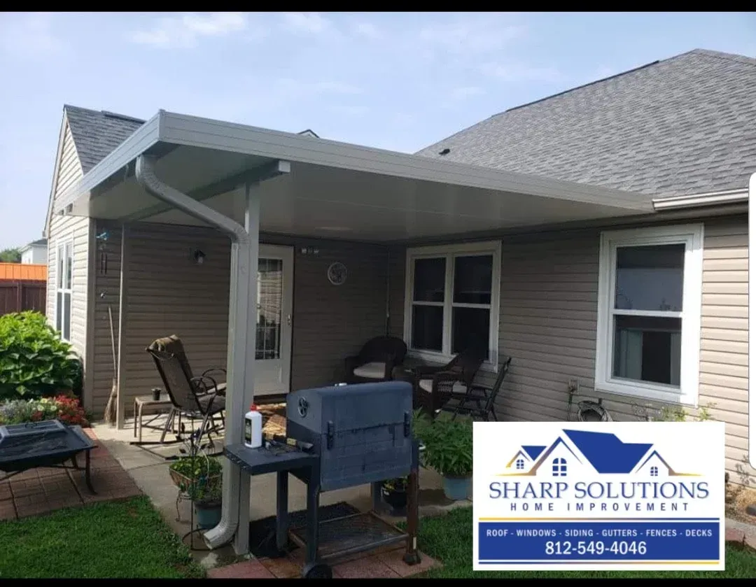 Patio with covered porch, grill, and chair beside a beige house; Sharp Solutions sign in front