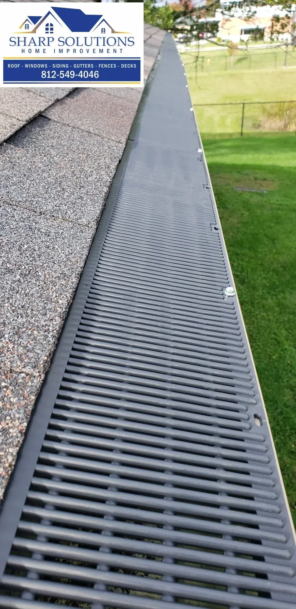 Black trench drain grate running beside gravel and grass along a paved edge outdoors