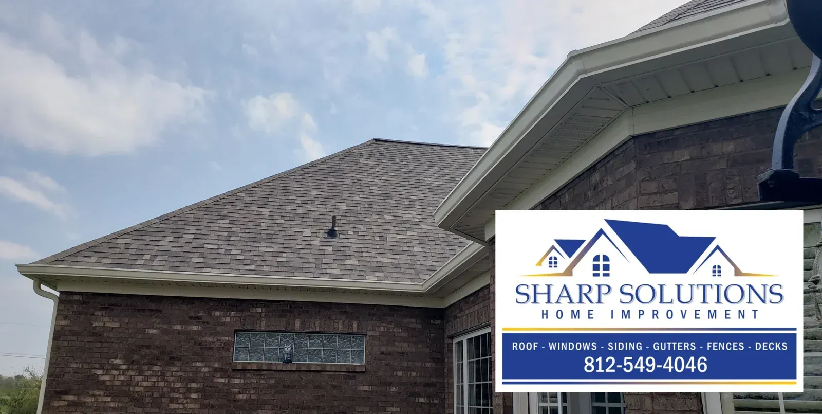 Roofing company sign on a brick house under a gray shingled roof