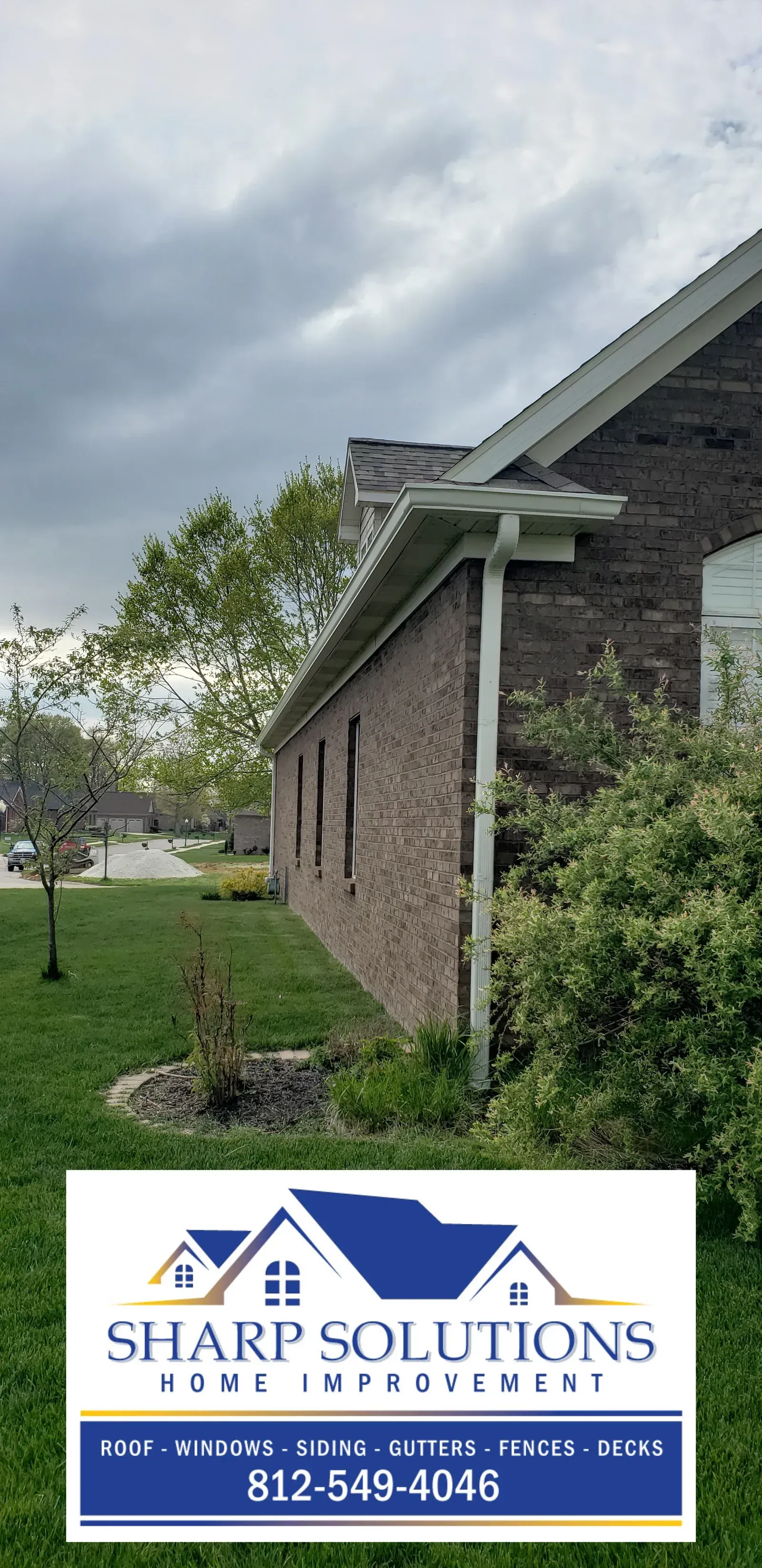 Brick house exterior with white trim, cloudy sky, green lawn, and Sharp Solutions cleaning service sign.