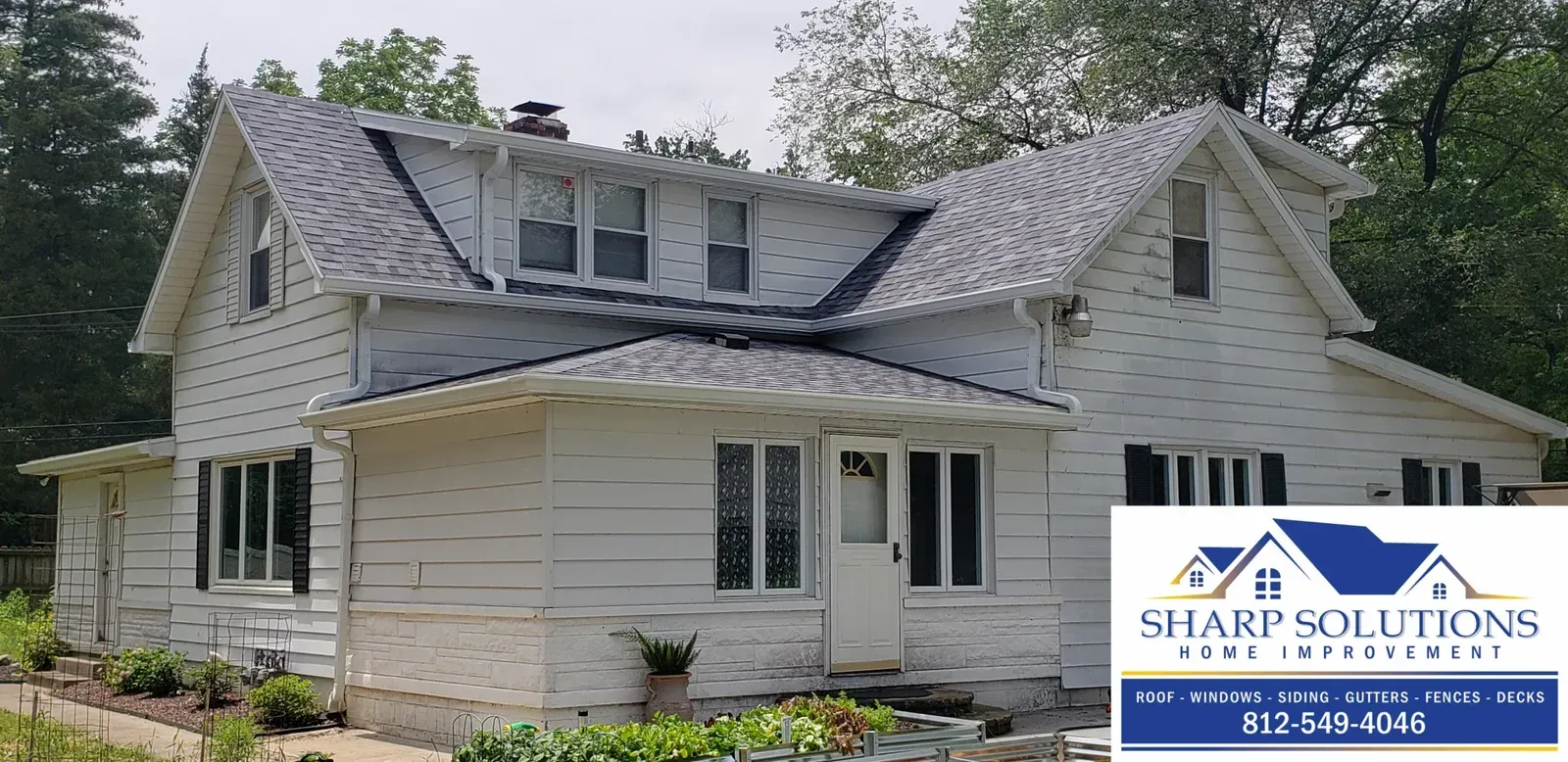 White two-story house with gray roof and dormer windows, exterior under renovation by Sharp Solutions Roofing.