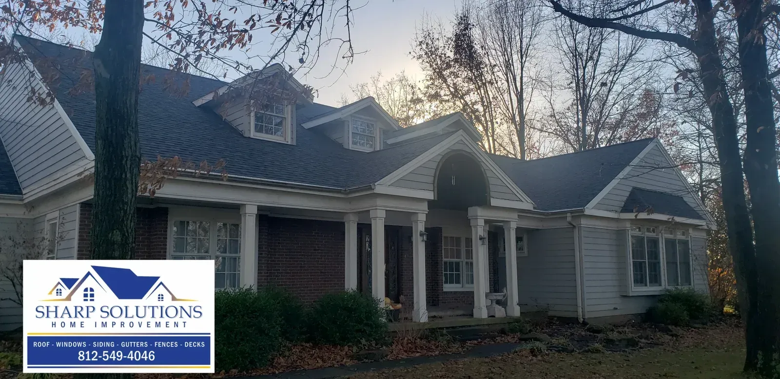 Two-story gray house with white trim and a front porch at dusk, with a real estate sign in front