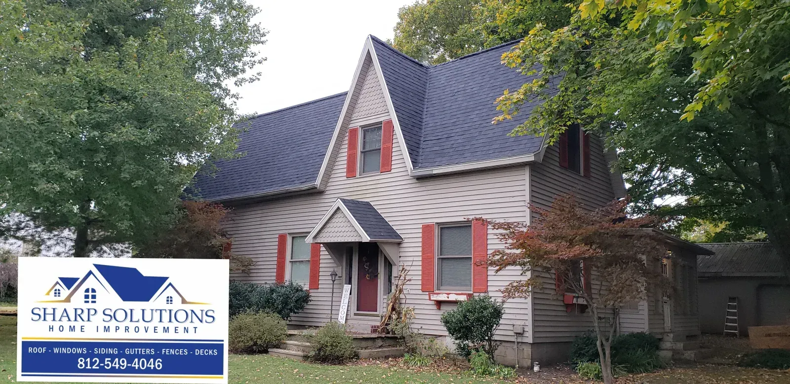 House with gray roof and red shutters, partially covered by a Sharh Solutions real estate sign