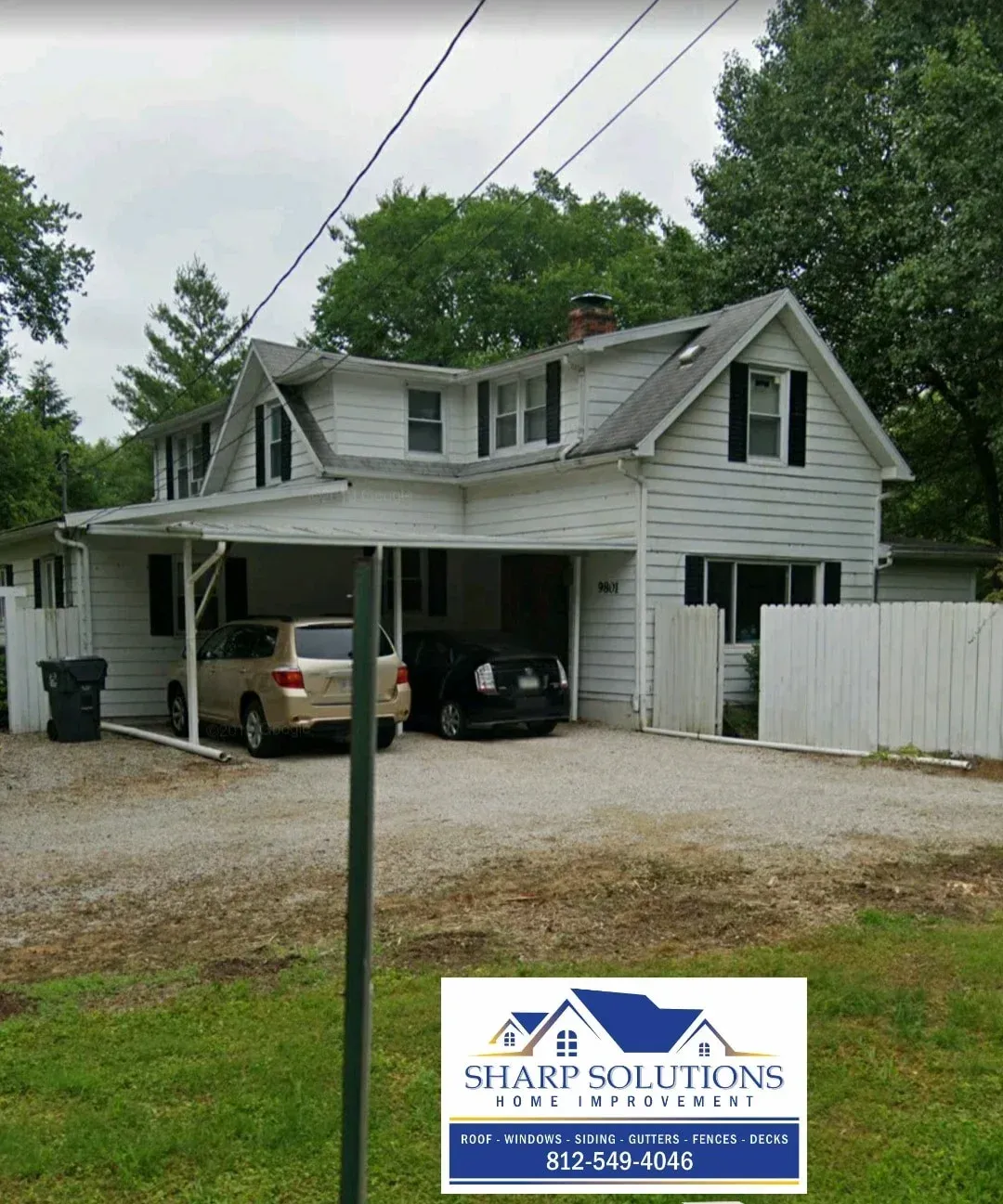 Two-story gray house with cars under carport, white fence, and a Shank Solutions sign in front.
