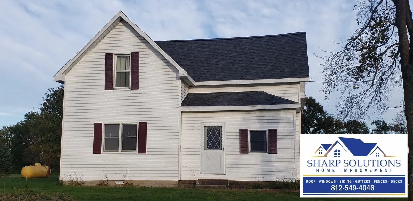 White two-story house with dark roof and maroon shutters, next to a Blair Solutions sign in a grassy yard