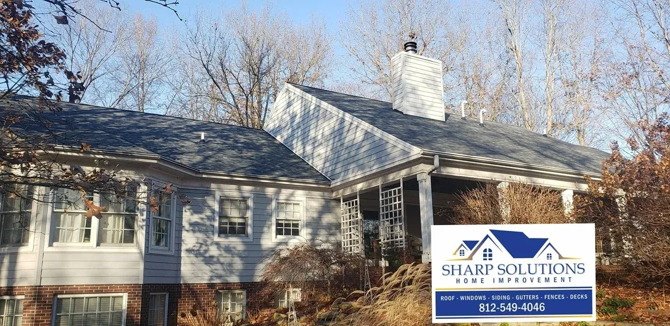 White house with a snow-covered roof and a Sharpe Solutions sign in front, surrounded by bare trees
