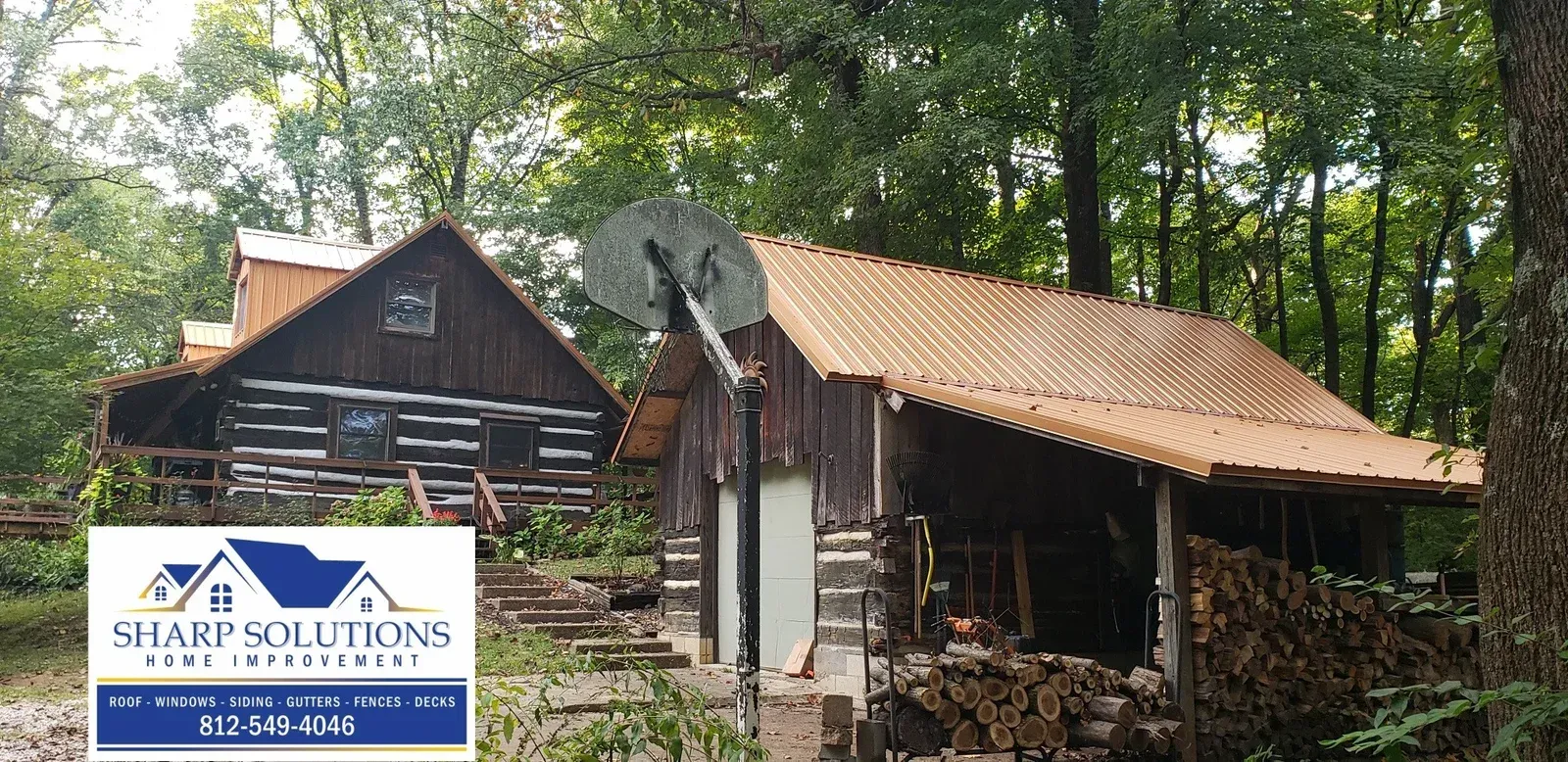 Old wooden cabin with rusted metal roof in a wooded area, with a Sharp Solutions sign in front