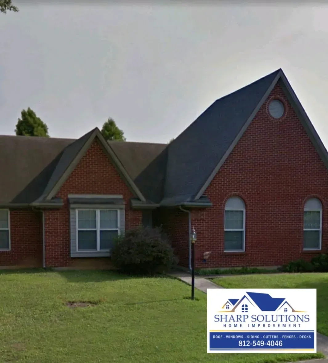 Red brick house with dark roof, white-trimmed windows, and a front lawn under a gray sky.