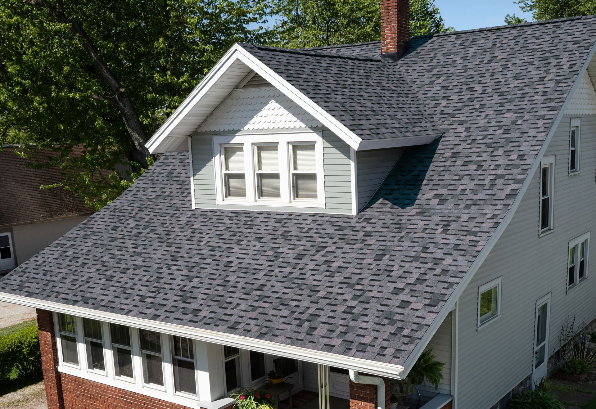 White house with gray shingled roof and dormer windows, viewed from above among trees