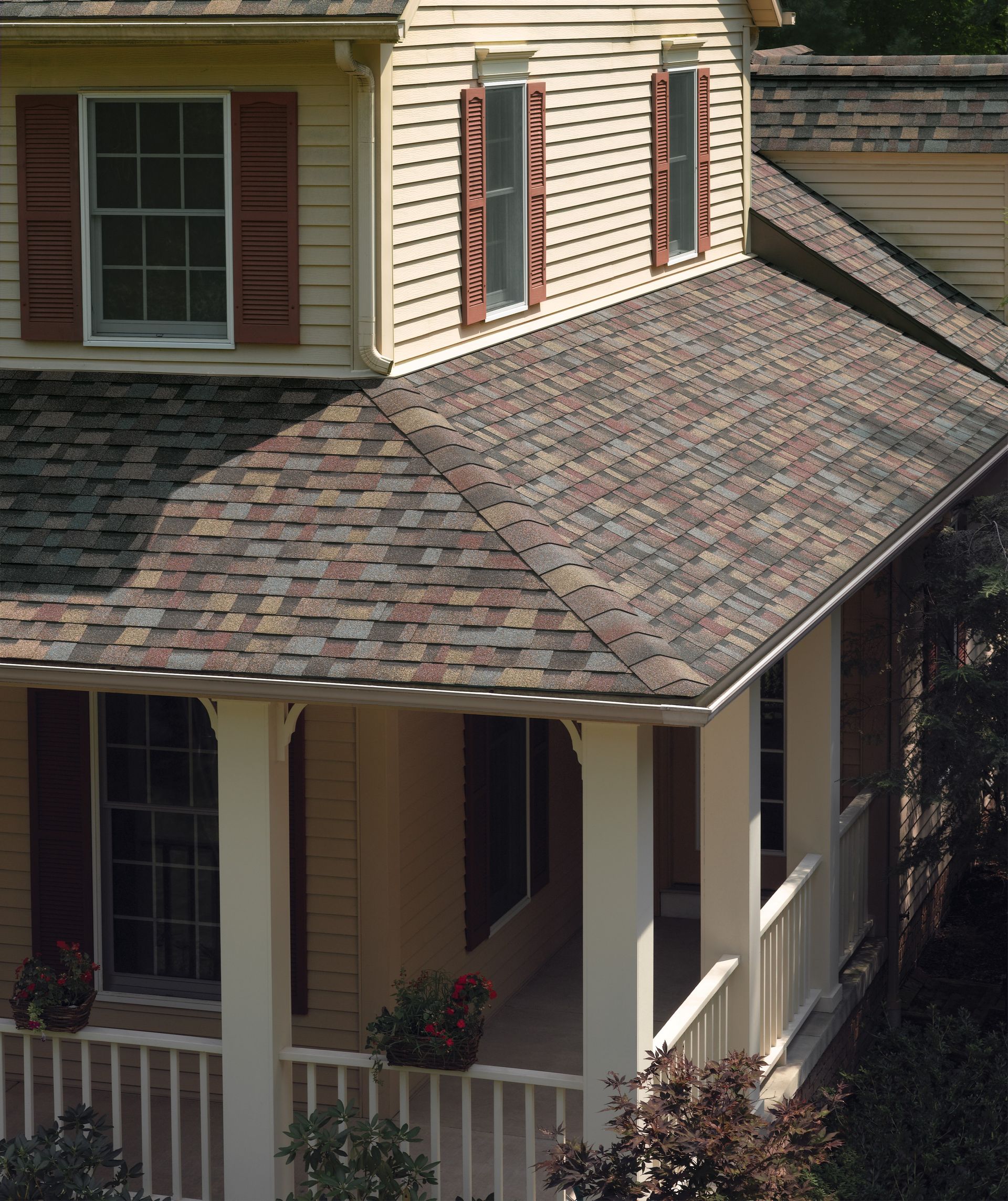 Front porch and roof of a beige house with maroon shutters and potted flowers