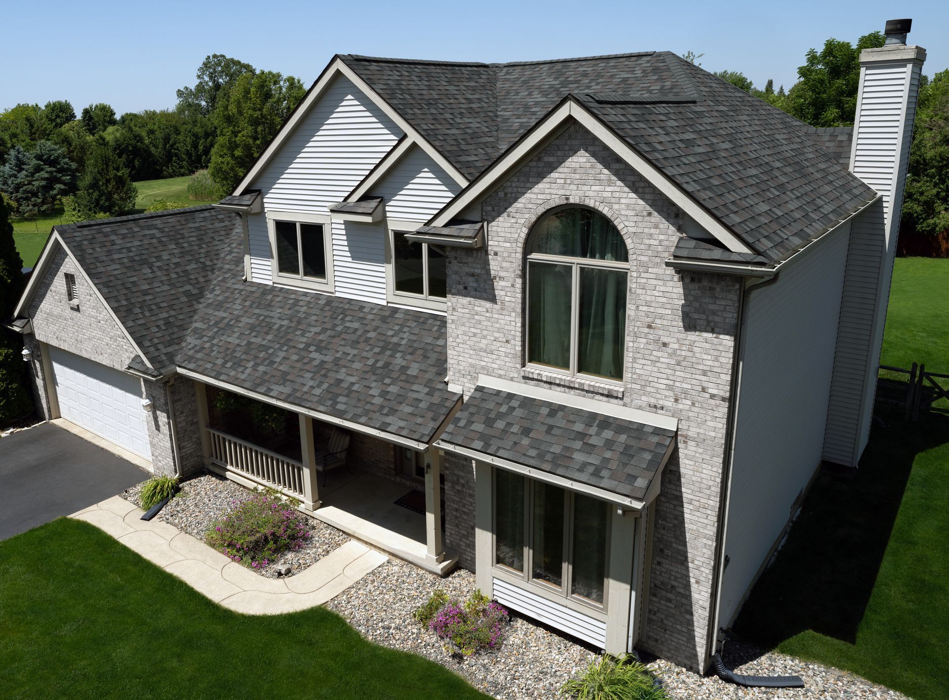 Two-story gray house with dark shingle roof, front porch, and lawn