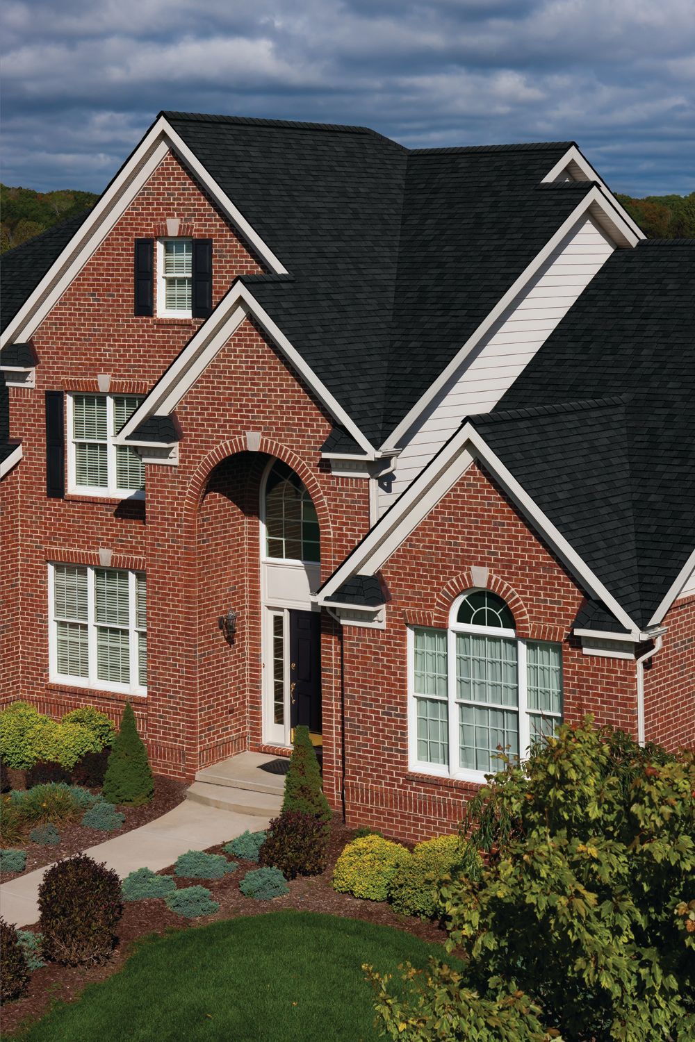 Brick house with dark gray roof, white trim, and a landscaped front yard under a cloudy sky