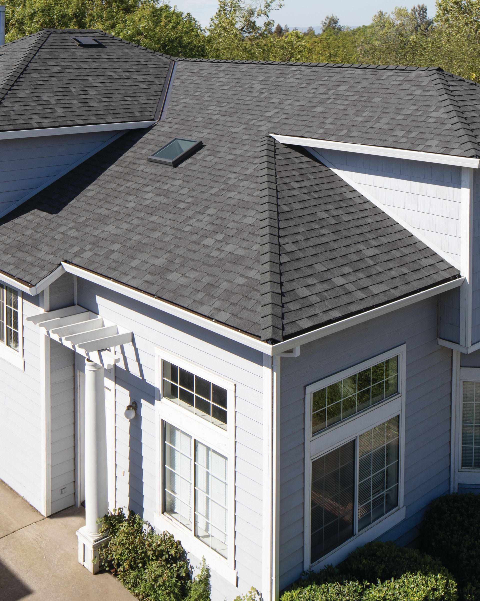 White house with dark gray shingle roof and large windows, viewed from above.